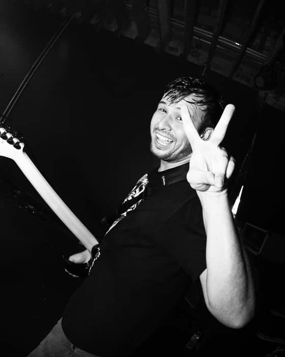 Chucky Guzman on stage, grinning and throwing a peace sign, guitar in hand